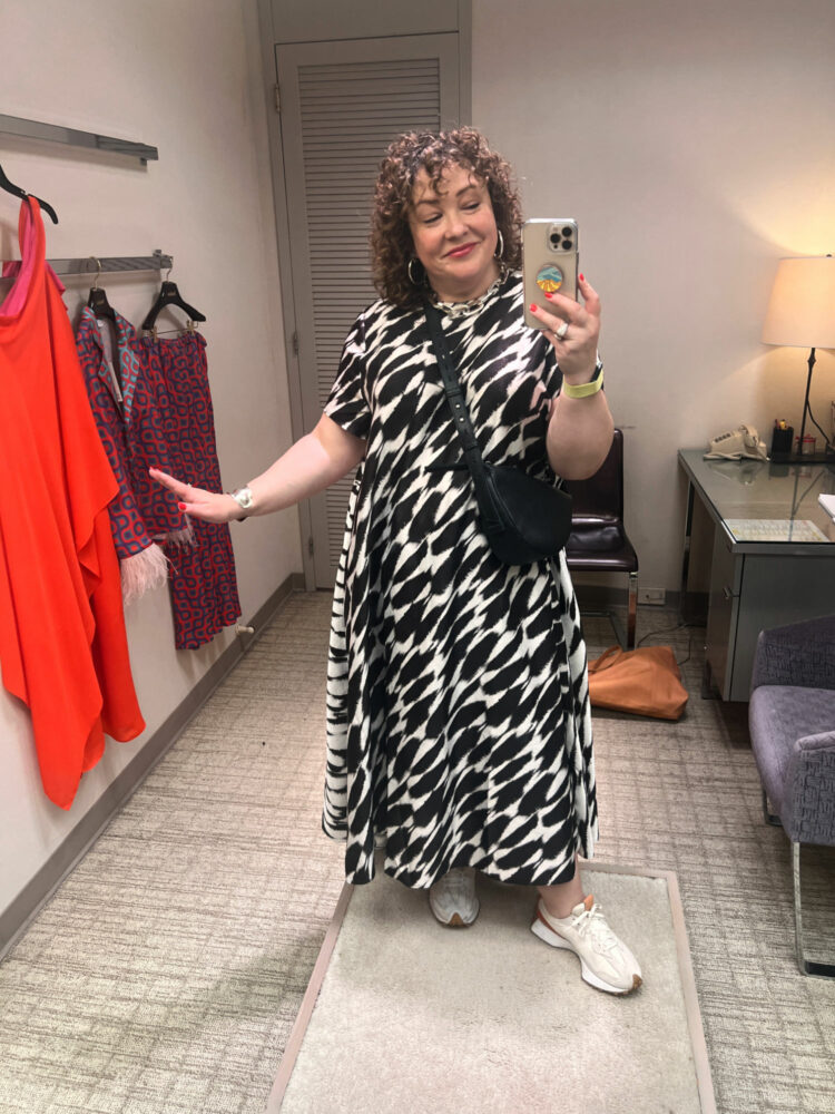 Alison standing in a fitting room, wearing a brown and ivory print Aurelia dress from Banana Republic with New Balance 327 sneakers and a The Sak black leather crossbody bag