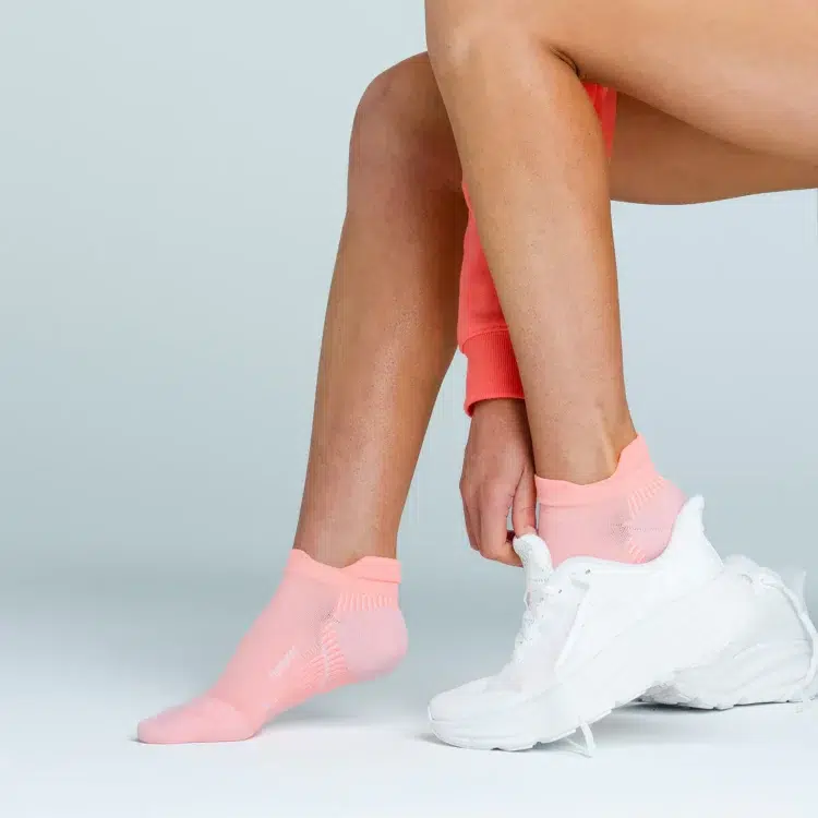 a woman wearing peach colored Feetures plantar fasciitis ankle socks, putting on a pair of white sneakers