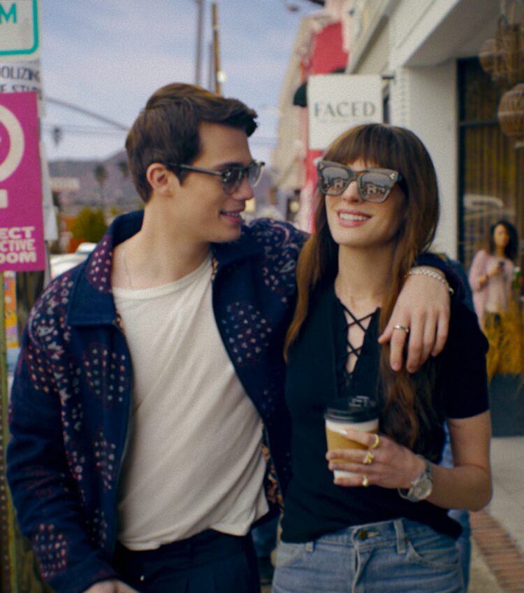 Hayes and Solene walking on a boardwalk laughing, drinking coffee, arm around Solene in the film The Idea of You
