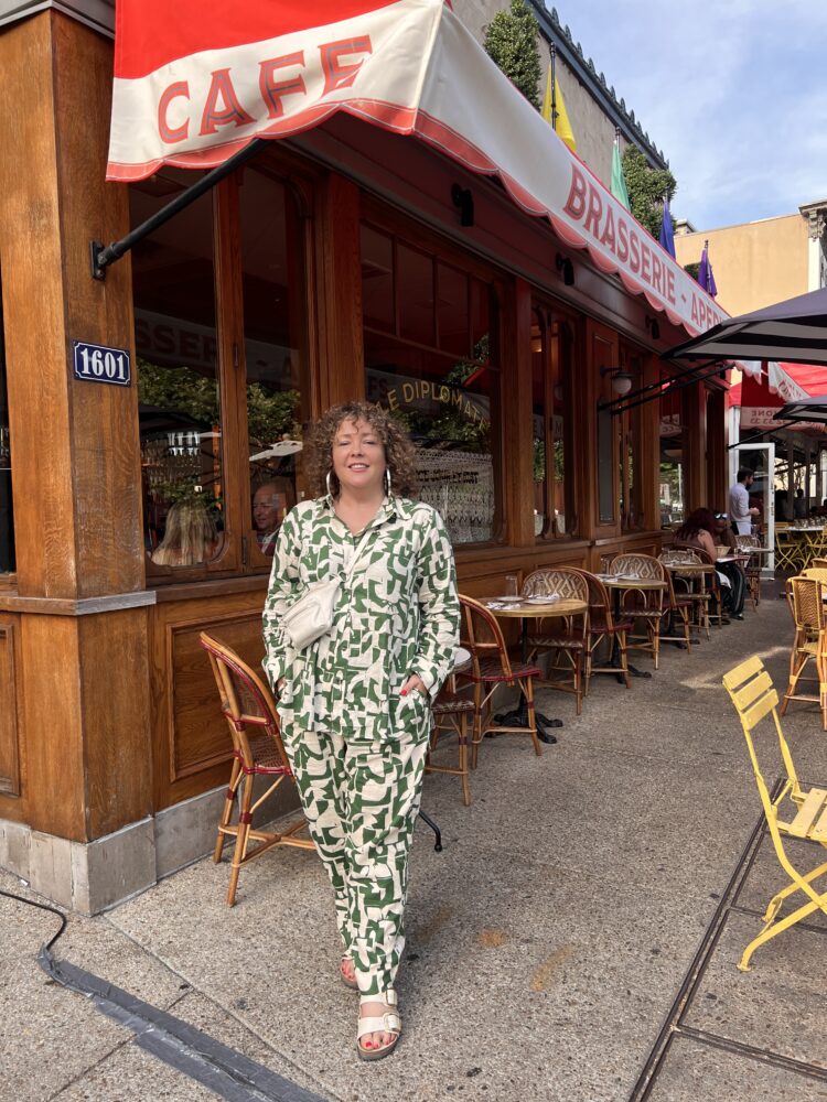 Alison Gary of Wardrobe Oxygen in front of the DC restaurant Le Diplomate, wearing a green and white print linen button-front tunic and matching pants from Universal Standard