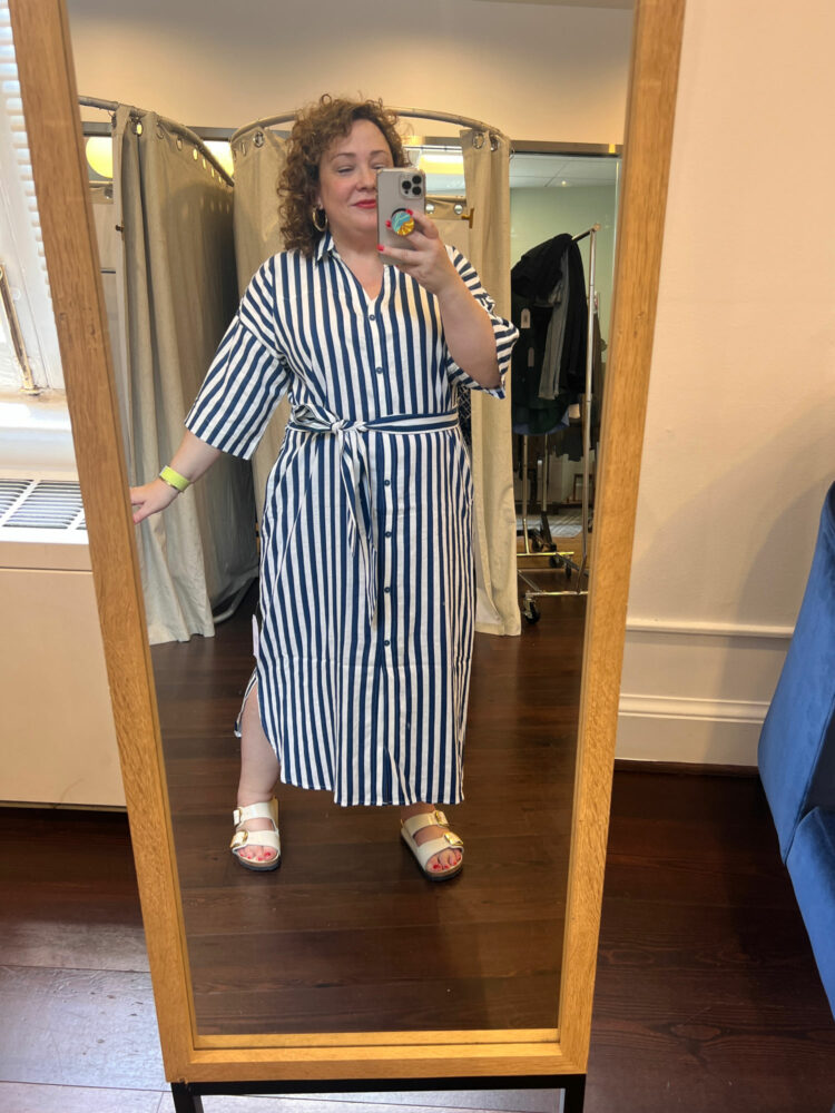 Alison Gary of Wardrobe Oxygen in a navy and white striped ankle-length short sleeve linen shirtdress with a self belt. She is taking a mirror selfie at the DC stop for the Universal Standard US on Tour trunk show