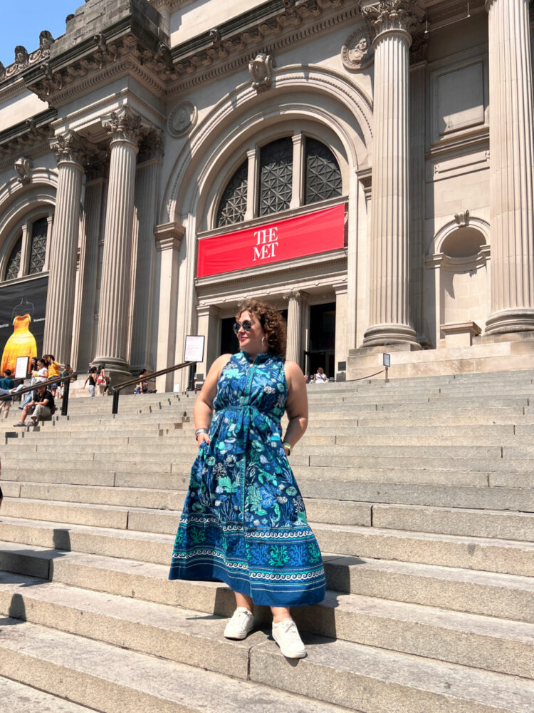 Alison Gary of Wardrobe Oxygen in a blue printed sleeveless Printdresh dress and white Birkenstock Bend sneakers on the steps of the Met in NYC.