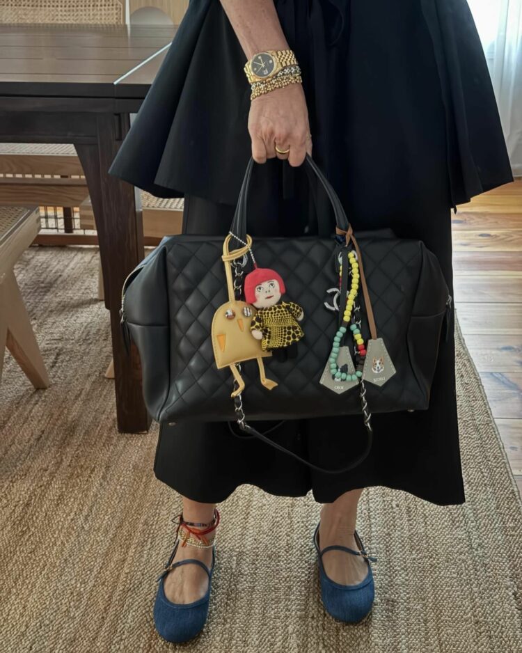 A woman over 40 holding a quilted black leather bag decorated with bag charms including a cartoon version of artist Yayoi Kusama