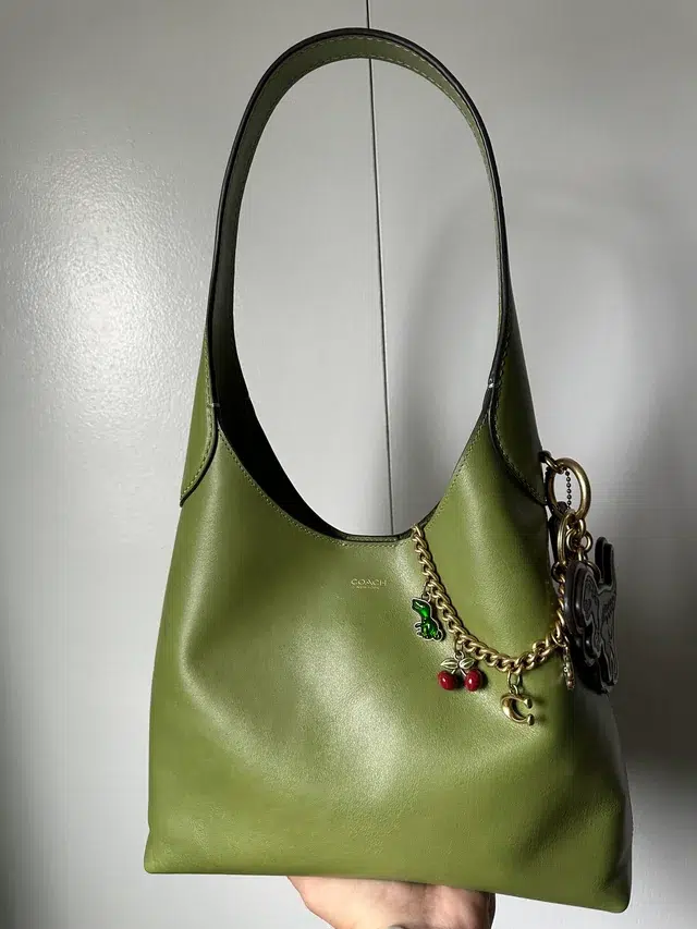 a green Coach Brooklyn 28 bag with Coach bag charms off the side