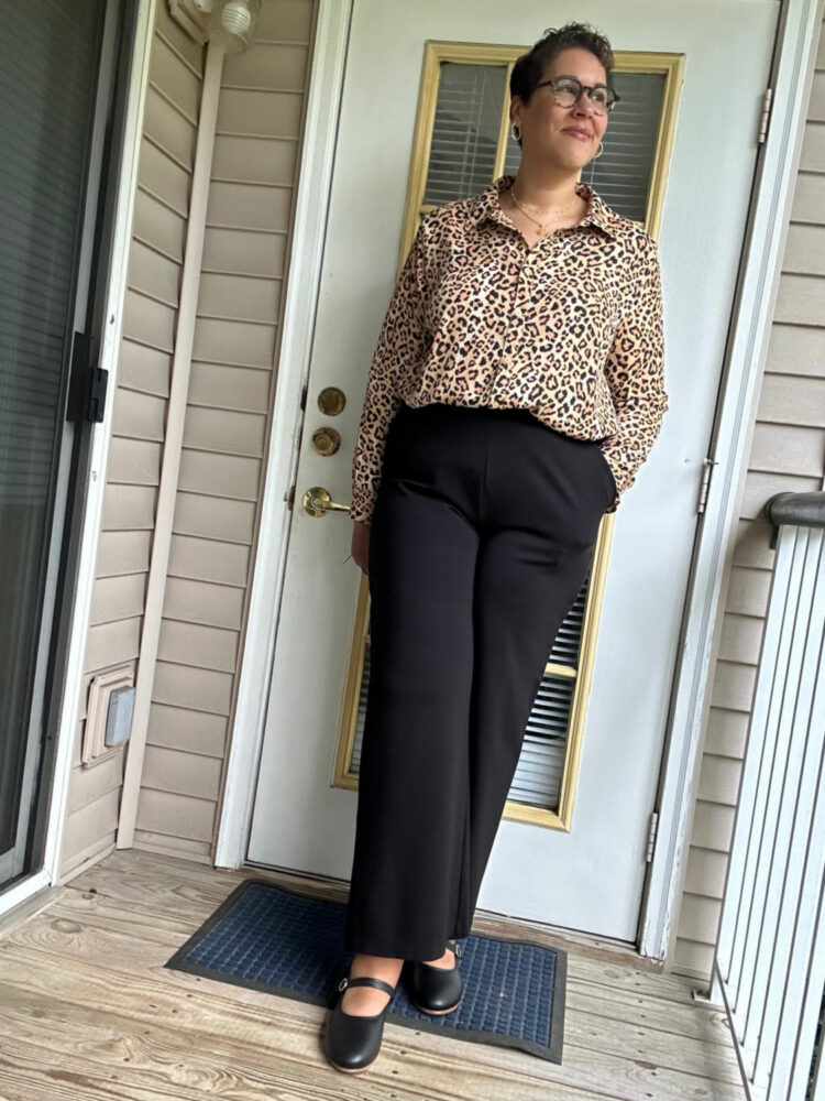 Woman in a leopard print button-front shirt tucked into black ponte trousers with black leather Mary Jane flats