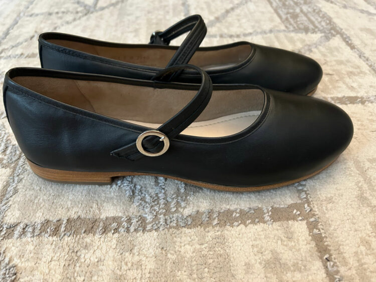 A side view of a pair of black leather Mary Janes from Poppy Barley with gold buckles and a subtle wood heel