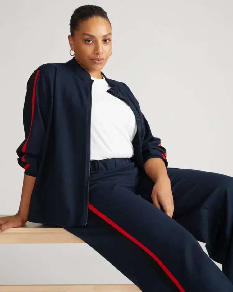 woman in a white t-shirt and Universal Standard navy ponte bomber jacket and Stephanie wide-leg pants in the navy with vermillion and black track stripes.