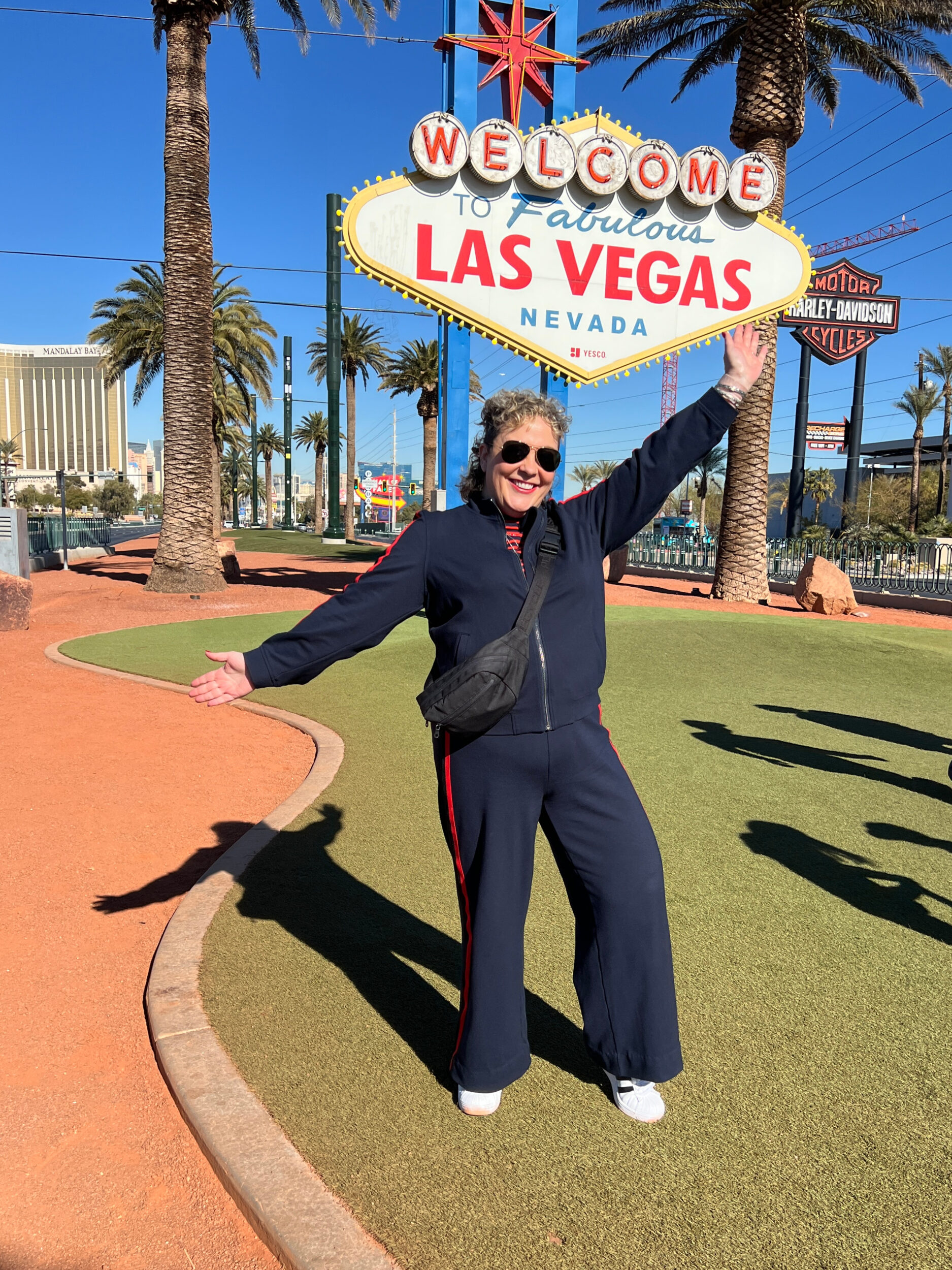 Alison Gary in a navy ponte track suit standing at the Welcome to Las vegas sign