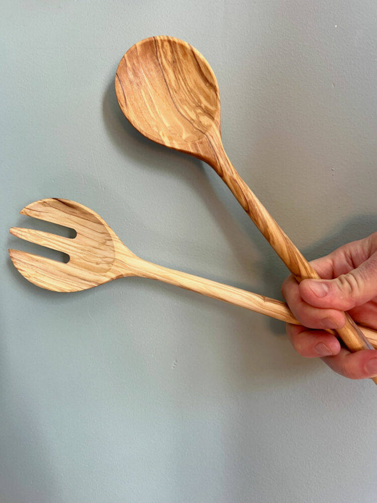 a hand holding olivewood salad servers